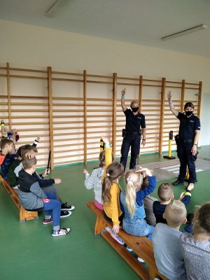 Policjantki z dziećmi pokazujące elementy odblaskowe na rękach