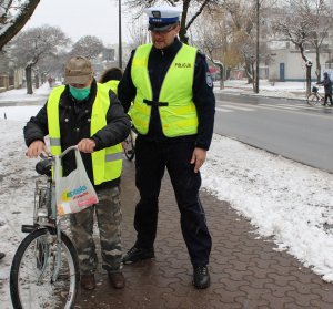 Policjant pomagający rowerzyście założyć kamizelkę odblaskową.