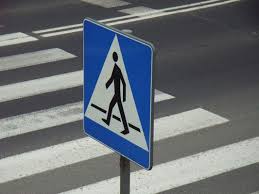 Na zdjęciu przejście dla pieszych i znak drogowy informujący o tym, że kierujący zbliża się do przejścia.