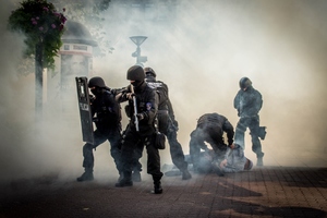 Policjanci podczas dynamicznej sytuacji, z tarczami i bronią, wśród dymu.