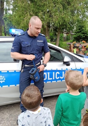 Policjant rozmawia z dziećmi stojąc obok radiowozu.