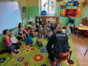 Policjant rozmawia z dziećmi zebranymi w sali przedszkolnej.