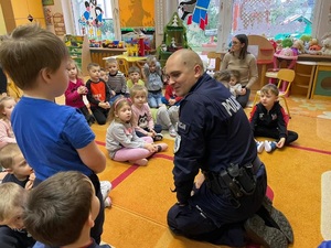 Policjant w sali przedszkolnej, rozmawia z dziećmi o bezpieczeństwie.