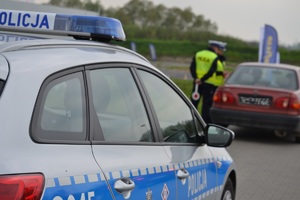 Policjant ruchu drogowego kontroluje kierowcę i pojazd, który jest zaparkowany przed radiowozem