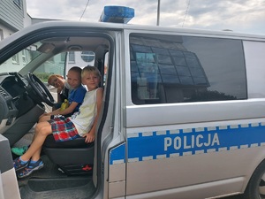 Dzieci siedzą w radiowozie policyjnym, pozują do zdjęć.