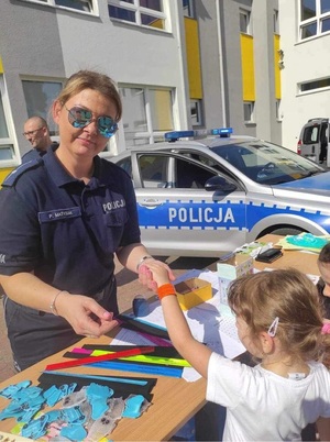 Policjantka rozdaje dzieciom opaski odblaskowe.
