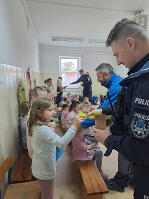 Policjanci z przedstawicielami marketu Mrówka rozdają dzieciom elementy odblaskowe.