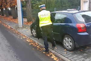 Policjant podszedł do zaparkowanego samochodu, rozmawia z kierującym, by dokonać kontroli drogowej
