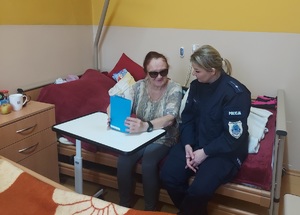 Policjantka wręcza kobiecie kartkę z życzeniami, siedzą razem na łóżku