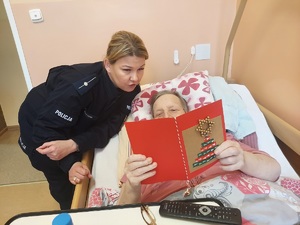 Policjantka wręcza kobiecie kartkę z życzeniami, kobieta leży na łóżku