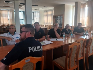 Aula w KPP Zduńska Wola. Przy wspólnym stole siedzą policjanci oraz strażnicy rybaccy.