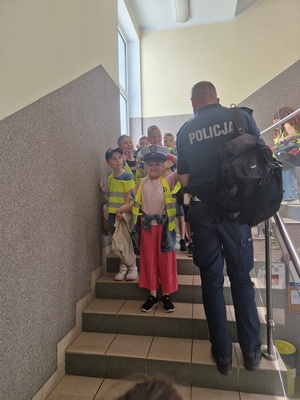 Dzieci zwiedzające budynek komendy i przymierzające czapkę policjanta wydziału ruchu drogowego.
