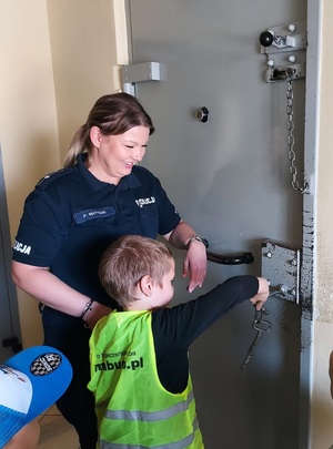 Policjantka pomaga chłopcu zamknąć kluczem drzwi pomieszczenia dla osób zatrzymanych.