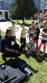 Starszy sierżant Bartosz Stelmasiak pokazuje dzieciom na pikniku profilaktycznym sprzęt służący do zabezpieczeń podczas imprez sportowych.