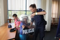 Sierżant sztabowy Kamila Sowińska prezentuje wyposażenie służbowe dzieciom.
