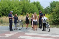 Policjanci rozmawiają z dziećmi przed szkoła i przekazują im odblaskowe elementy.