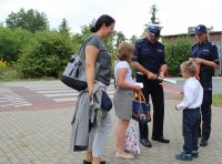 Policjanci rozmawiają z dziećmi przed szkołą i przekazują im odblaskowe elementy.