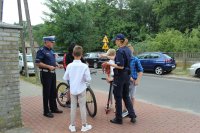 Policjanci rozmawiają z dziećmi przed szkołą i przekazują im odblaskowe elementy.