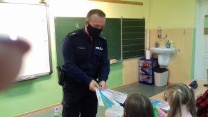 Policjant wręczający dzieciom opaski odblaskowe