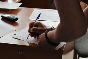 Osoba zatrzymana, ma założone kajdanki, podpisuje protokół.