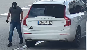 Na zdjęciu biały samochód marki volvo, widać obok pojazdu mężczyznę, który ma na głowie czarną czapkę z daszkiem, ciemną koszulkę typu t-shirt, długie spodnie koloru niebieskiego, czarne buty, na lewej ręce ma zegarek. Widać tablice rejestracyjne o  numerze: DWL AJ57.
