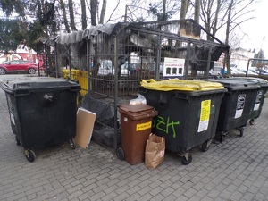 Spalona pergola śmietnikowa, widać spalony dach i wokół pergoli stojące kontenery na śmieci.