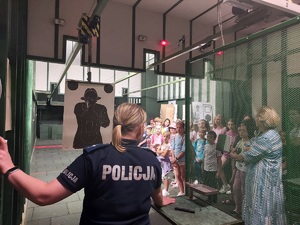 Policjantka na strzelnicy, tłumaczy dzieciom jak wygląda strzelanie w tym pomieszczeniu