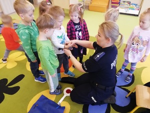 Policjantka pokazuje dzieciom kajdanki i demonstruje jak się je zakłada.