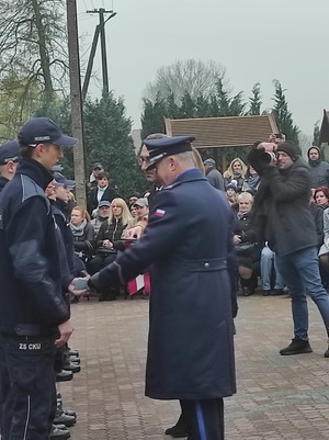 Komendant Powiatowy Policji w Zduńskiej Woli, razem z dyrektorem szkoły, wręczają uczniom legitymacje, gratulują.