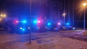 Przed budynkiem Komendy Powiatowej Policji w Zduńskiej Woli są radiowozy z włączonymi sygnałami świetlnymi. Obok pojazdów stoją policjanci salutując.