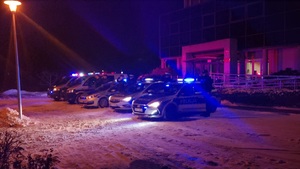 Przed budynkiem Komendy Powiatowej Policji w Zduńskiej Woli są radiowozy z włączonymi sygnałami świetlnymi. Obok pojazdów stoją policjanci salutując.