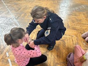 Policjanta kuca na podłodze razem z dziewczynką, która spłata dłonie, by uchronić je w przypadku ataku psa.