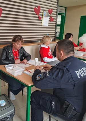 Policjant siedzi przy stoliku na wprost kobiety, która pomaga w wypełnianiu dokumentacji rejestracyjnej