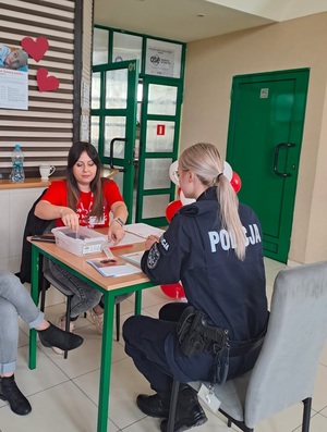 Policjantka siedzi przy stoliku na wprost kobiety, która pomaga w wypełnianiu dokumentacji rejestracyjnej