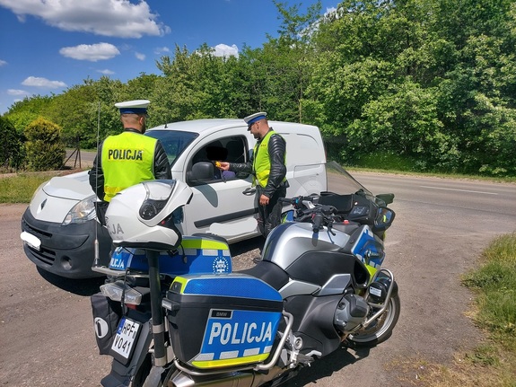 Dwaj policjanci, obok stoją służbowe motocykle, jeden z nich podszedł do kierowcy i na urządzeniu bada stan trzeźwości kierującego.