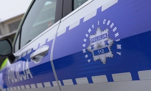 Fragment radiowozu, na karoserii napis Policja oraz policyjna odznaka i napis: Pomagamy i chronimy