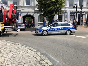 Radiowóz policyjny stoi zaparkowany na wjeździe na rondo. W tle widać osoby przyglądające się wypadkowi.
