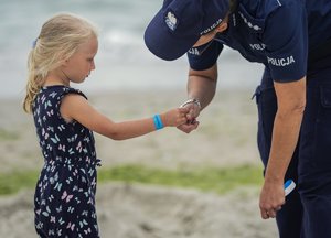 Policjant stoi przed dziewczynką, trzyma ją za rękę.