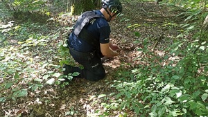 Umundurowany policjant, w lesie, ogląda granat