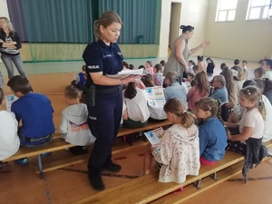 Policjantka rozdająca książeczki edukacyjne dzieciom biorącym udział w półkoloniach.