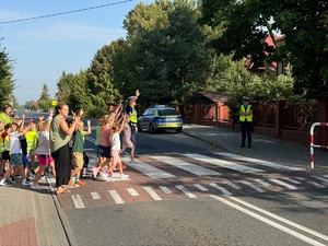 Dzieci przechodzące przez przejście dla pieszych pod nadzorem policjanta z ruchu drogowego.