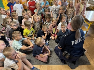 Policjantka siedząca z dziećmi na podłodze i omawiająca zagadnienia związane z bezpieczeństwem.