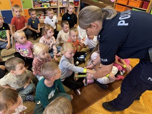 Policjantka rozdająca dzieciom elementy odblaskowe.