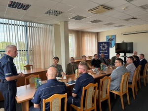 Aula zduńskowolskiej komendy. Przy długim stole, siedzą uczestnicy spotkania. W szczycie stołu siedzi gospodarz - zduńskowolski komendant.