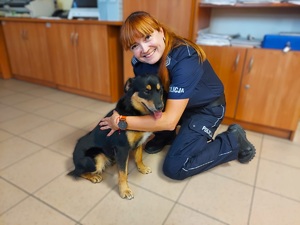 Policjantka klęka przy psie, obejmuje go, przytula.