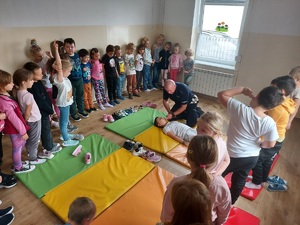 Policjant pokazuje dzieciom jak udzielać pierwszej pomocy.