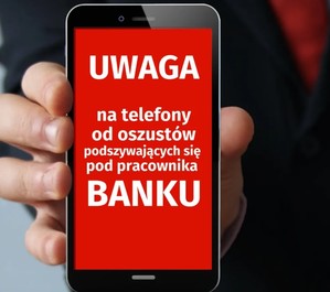 Ręka trzyma telefon komórkowy. Na nim wyświetla się grafika - napis: Uwaga na telefony od oszustów podszywających się pod pracownika banku.