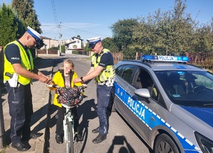 Policjanci dają osobie na rowerze elementy odblaskowe.