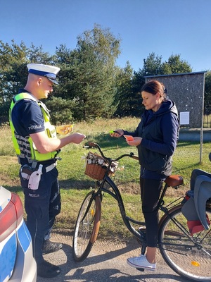 Policjanci dają kobiecie na rowerze elementy odblaskowe.