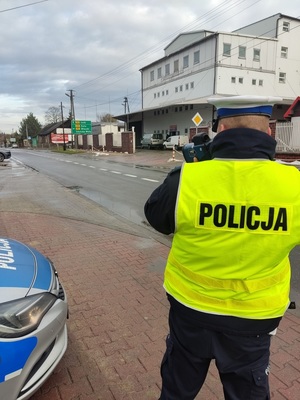 Policjant stoi tyłem do zdjęcia, mierzy prędkość jadących pojazdów.